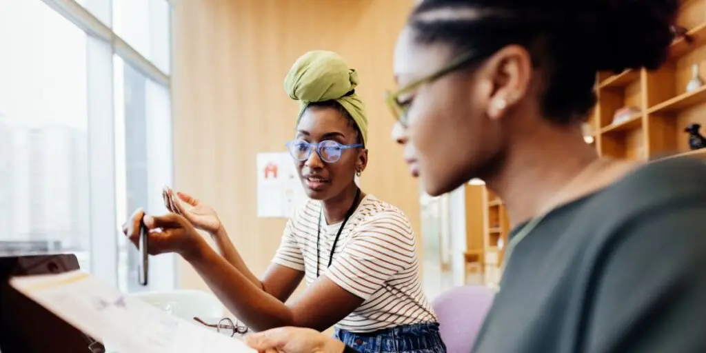 Image of two young people going over one of one of the woman's budget and teaching the other in a Financial Literacy.