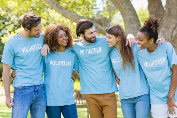 Image of 5 young adults wearing shirts that say Volunteer representing how local businesses can help break the cycle of poverty.