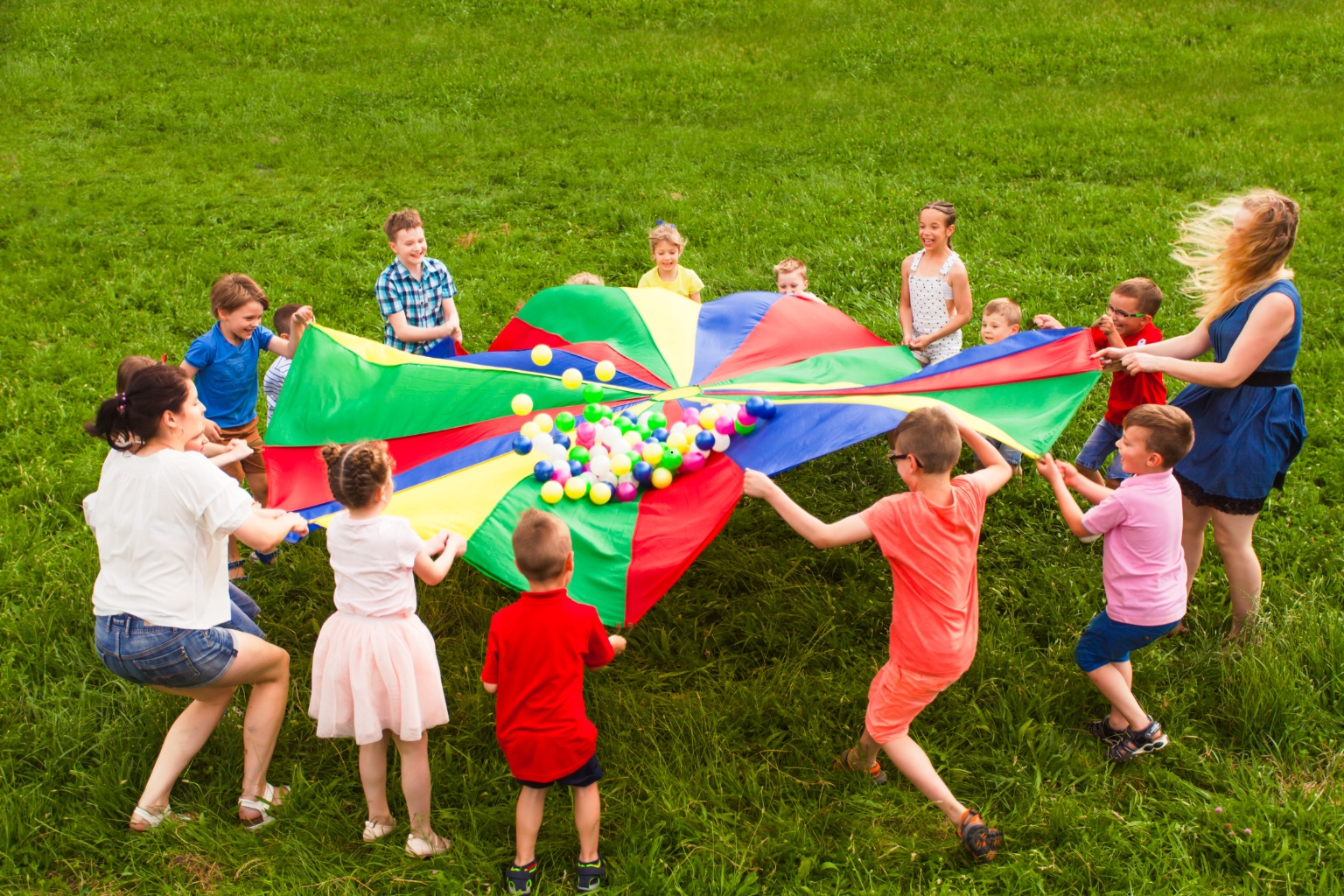 Image of kids playing with a giant parachute representing summer childcare struggles.